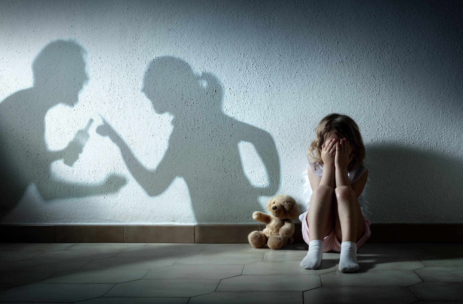 Adverse Childhood Experiences A little girl sat on the floor with face in her hands while there is the shadow of her parents arguing on the wall