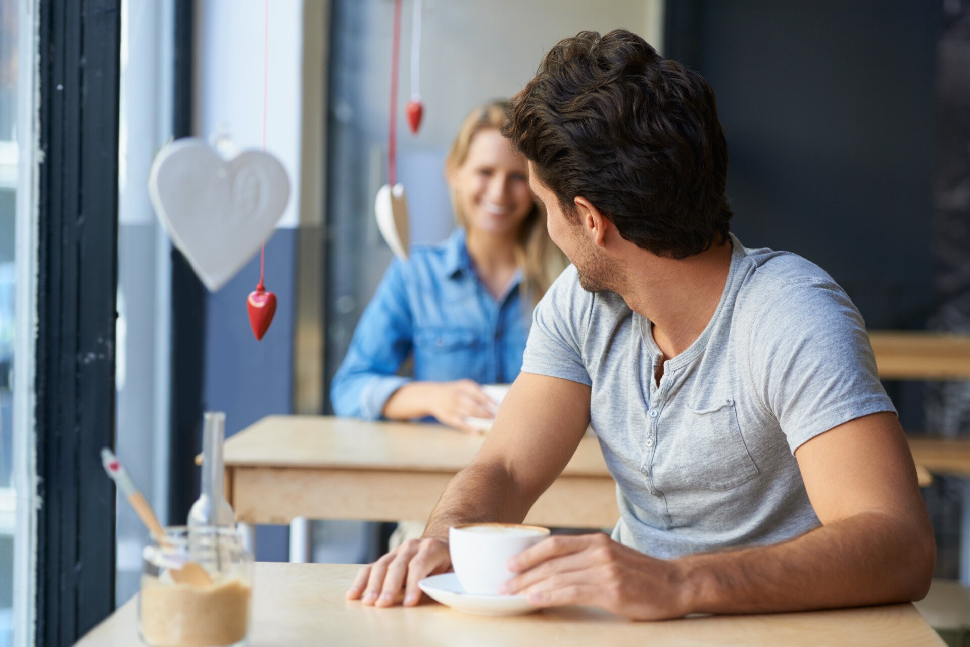 A man at a cafe turning around to flirt with a woman sat behind him.