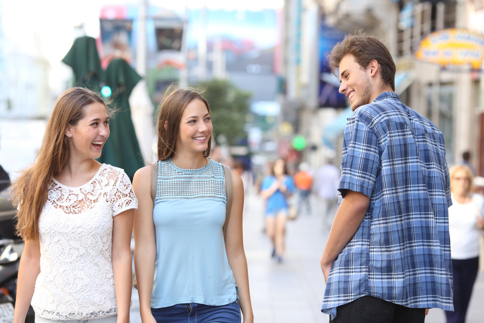 Man walking down the street and looking and smiling at two women walking in the opposite direction.