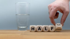 Framing Effect In Psychology 19 Hand turns a dice and changes the expression "half empty" to "half full" with a glass of water in the background