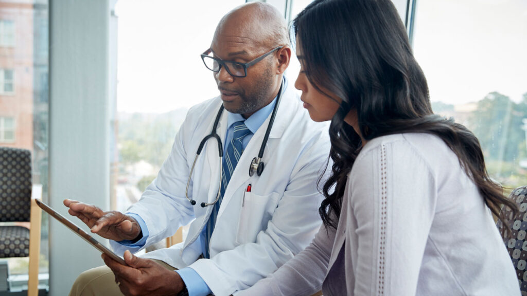 How to Spot Medical Gaslighting and What to Do About It 1 a male doctor talking to a female patient while looking at a digital tablet