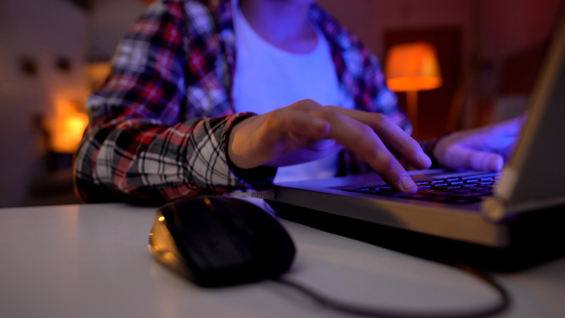 Online Radicalization Close up of a young person typing on their laptop in a dark room.