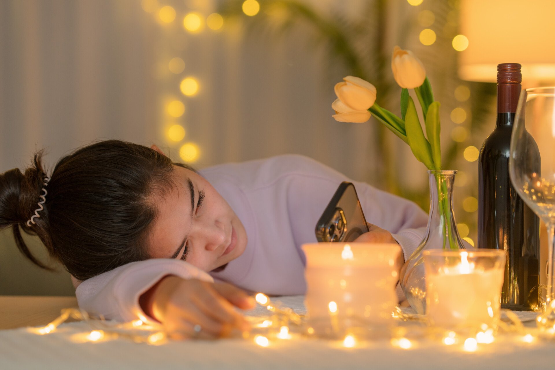 Single Girl A single girl lay with her head on the table looking at her phone. Candles and a bottle of wine on the table.